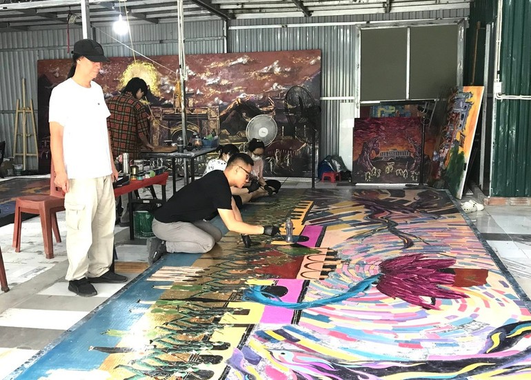 Painter Chu Nhat Quang working on the completion of the painting with feedback from his father, Meritorious Artist Chu Luong.