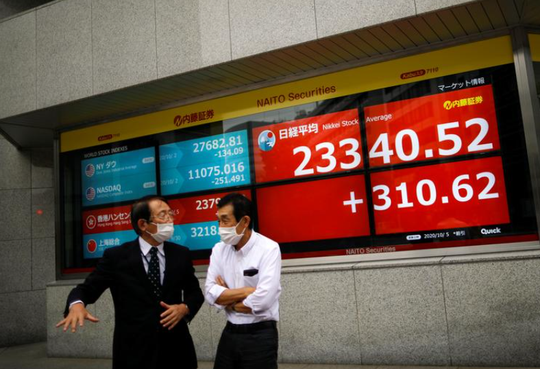 Men wearing protective face masks chat in front of a screen displaying Nikkei share average and world stock indexes outside a brokerage, amid the coronavirus disease (COVID-19) outbreak, in Tokyo, Japan October 5, 2020 (Photo: Reuters) 