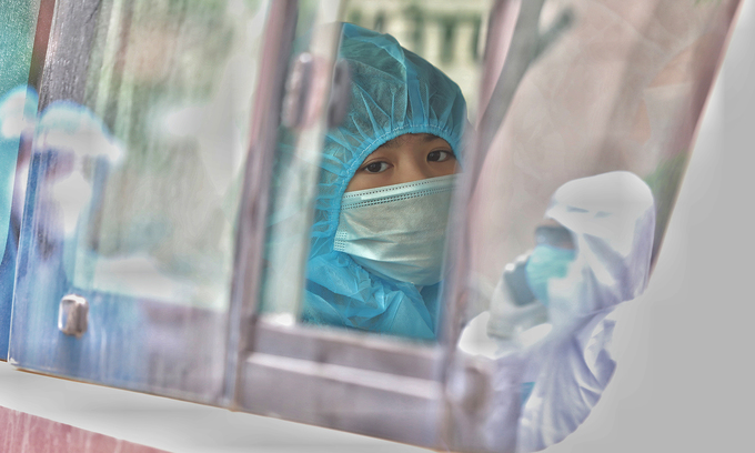 A person wears a protective suit on a bus at a Covid-19 locked down zone in Hanoi, with reflections of medical workers on the windows, May 13, 2021. Photo by VnExpress/Ngoc Thanh.