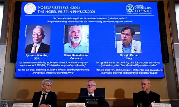 Nobel committee for physics members sit in front of a screen displaying 2021 winners (left to right) Syukuro Manabe, Klaus Hasselmann and Giorgio Parisi. Photograph: Jonathan Nackstrand/AFP/Getty Images