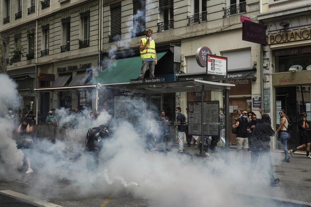 Protestors stand in smoke flares in front of policemen during a demonstration in Lyon, central France, Saturday, July 31, 2021. Demonstrators gathered in several cities in France on Saturday to protest against the COVID-19 pass, which grants vaccinated individuals greater ease of access to venues. (AP Photo/