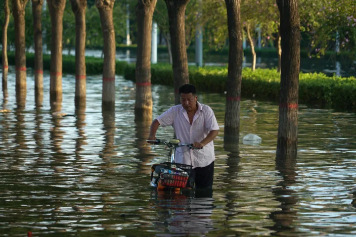 In this July 26, 2021, file photo, a man pushes a scooter through floodwaters in Xinxiang in central China's Henan Province, Monday, July 26, 2021. Chinese authorities have announced a huge jump in the death toll from recent floods. The Henan province government said Monday, Aug. 2, 2021, that over 300 have people died and at least 50 remain missing. (AP Photo/Dake Kang, File)