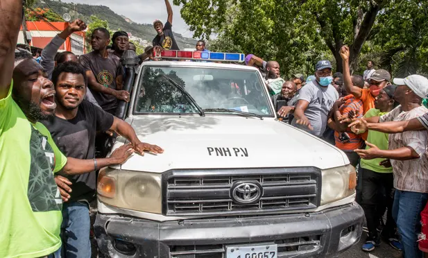 People cheer as a police car drives past the police station where men, accused of being involved in the assassination of President Jovenel Moise, are being held in Port au Prince Photograph: AFP/Getty Images